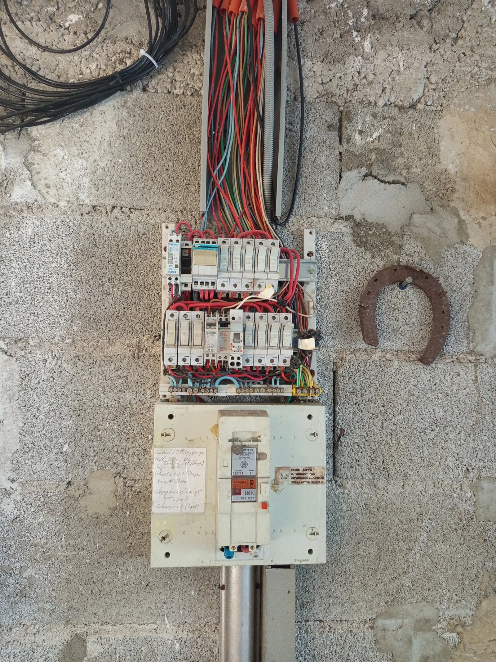 Ancien tableau électrique de M.A.S ELEC 30 : appareillage ancien et faisceau de fils apparents sur un mur en parpaing