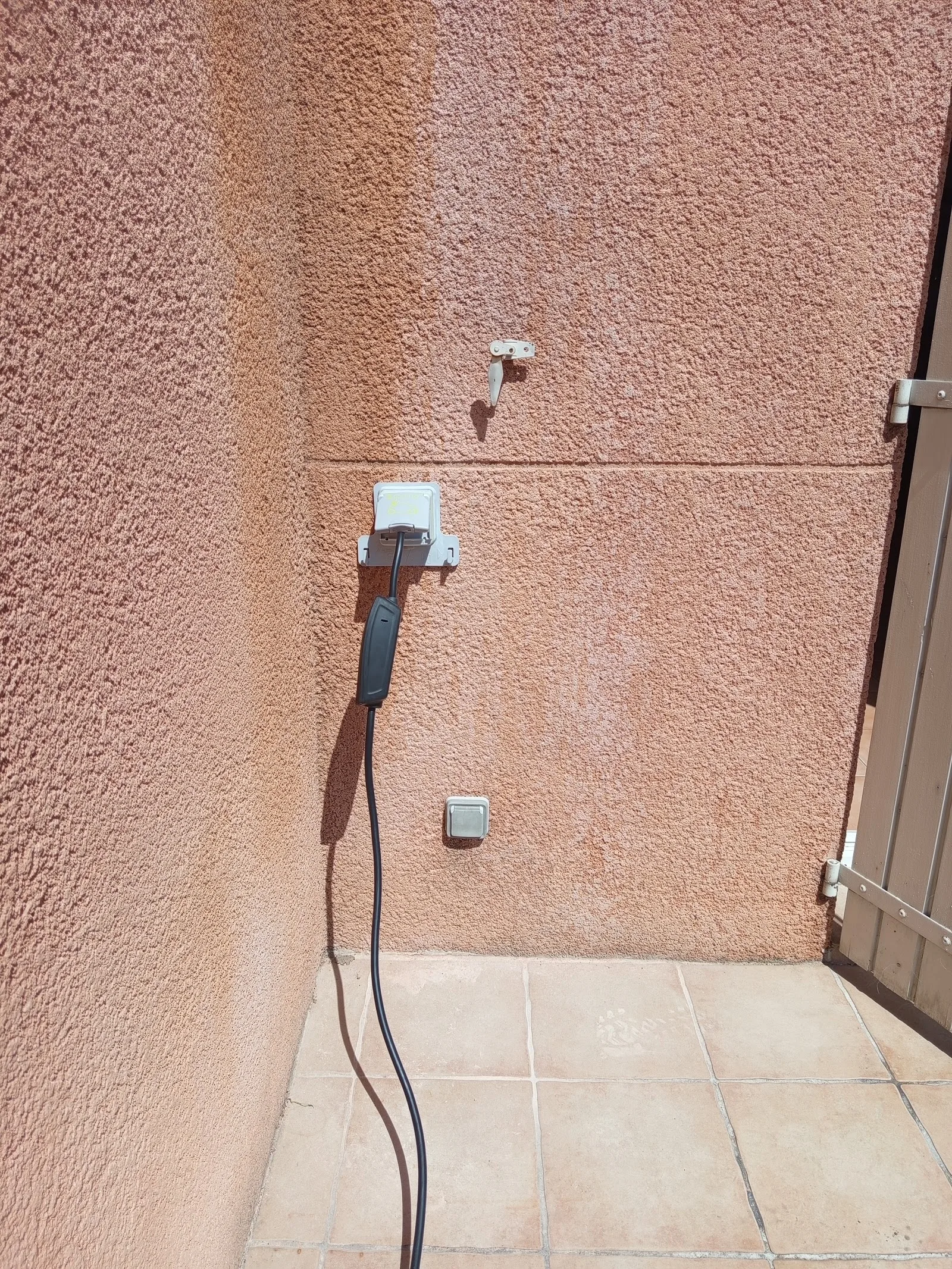 Prise extérieure étanche et câble de recharge branché sur un mur crépi, installés par M.A.S ELEC 30